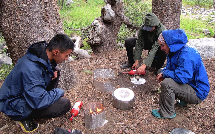 Three outward bound students use camping stoves to prepare food. 